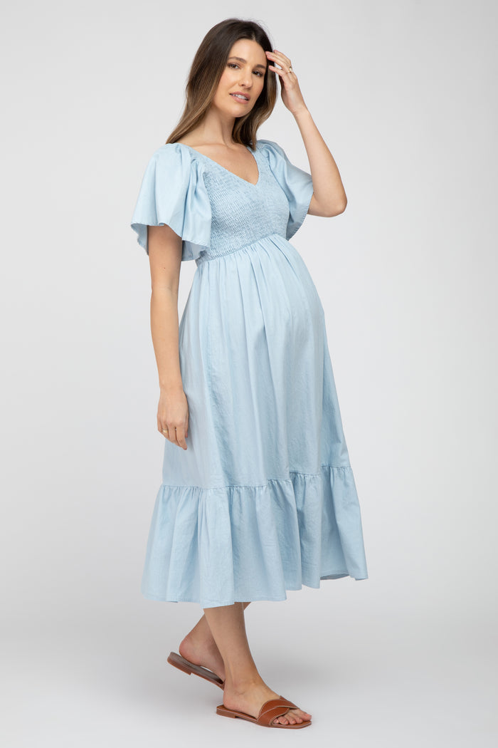 woman wearing a light blue maternity dress with short flounce sleeves and a ruffled hem, displaying her baby bump