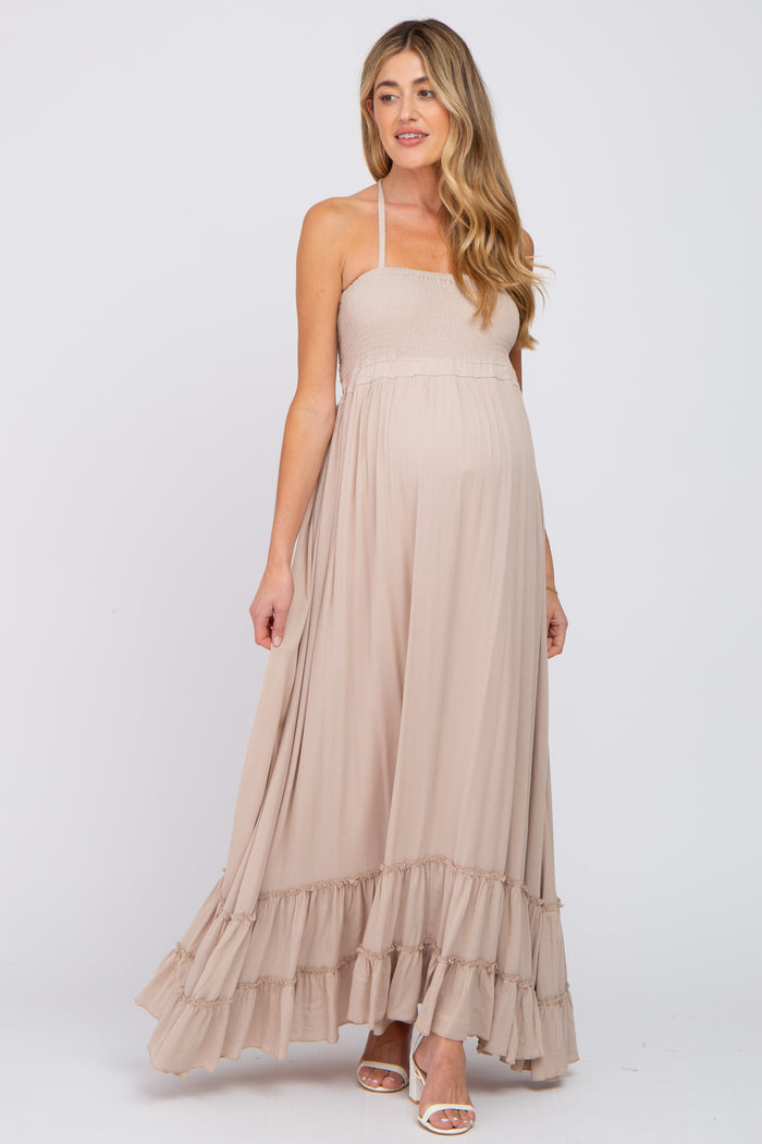 pregnant woman wearing a beige smocked halter maternity maxi dress with ruffle hem and white heels