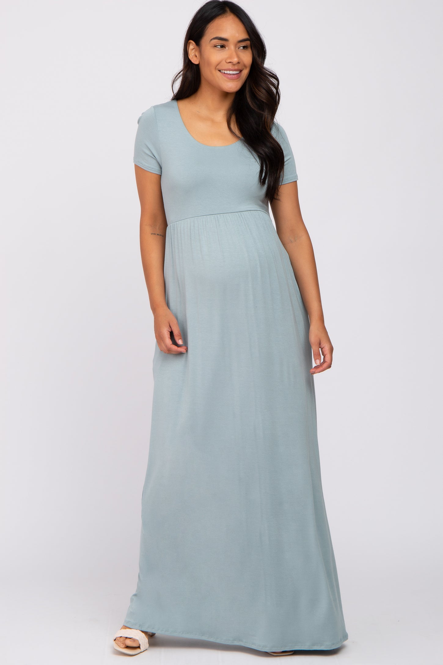smiling pregnant woman wearing a light blue short sleeve maternity maxi dress against a white background