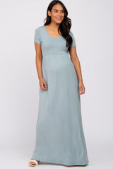 smiling pregnant woman wearing a light blue short sleeve maternity maxi dress against a white background