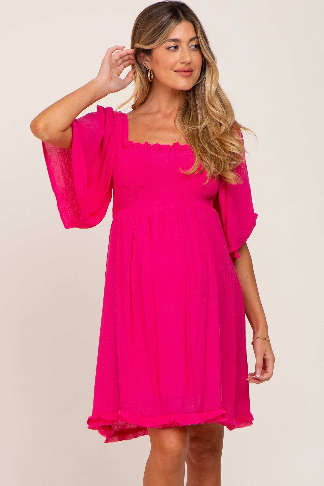 woman wearing a hot pink smocked maternity dress with flutter sleeves and a square neckline