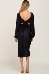 Back view of a woman wearing a black pleated midi dress with long sleeves and a tie-back cutout detail