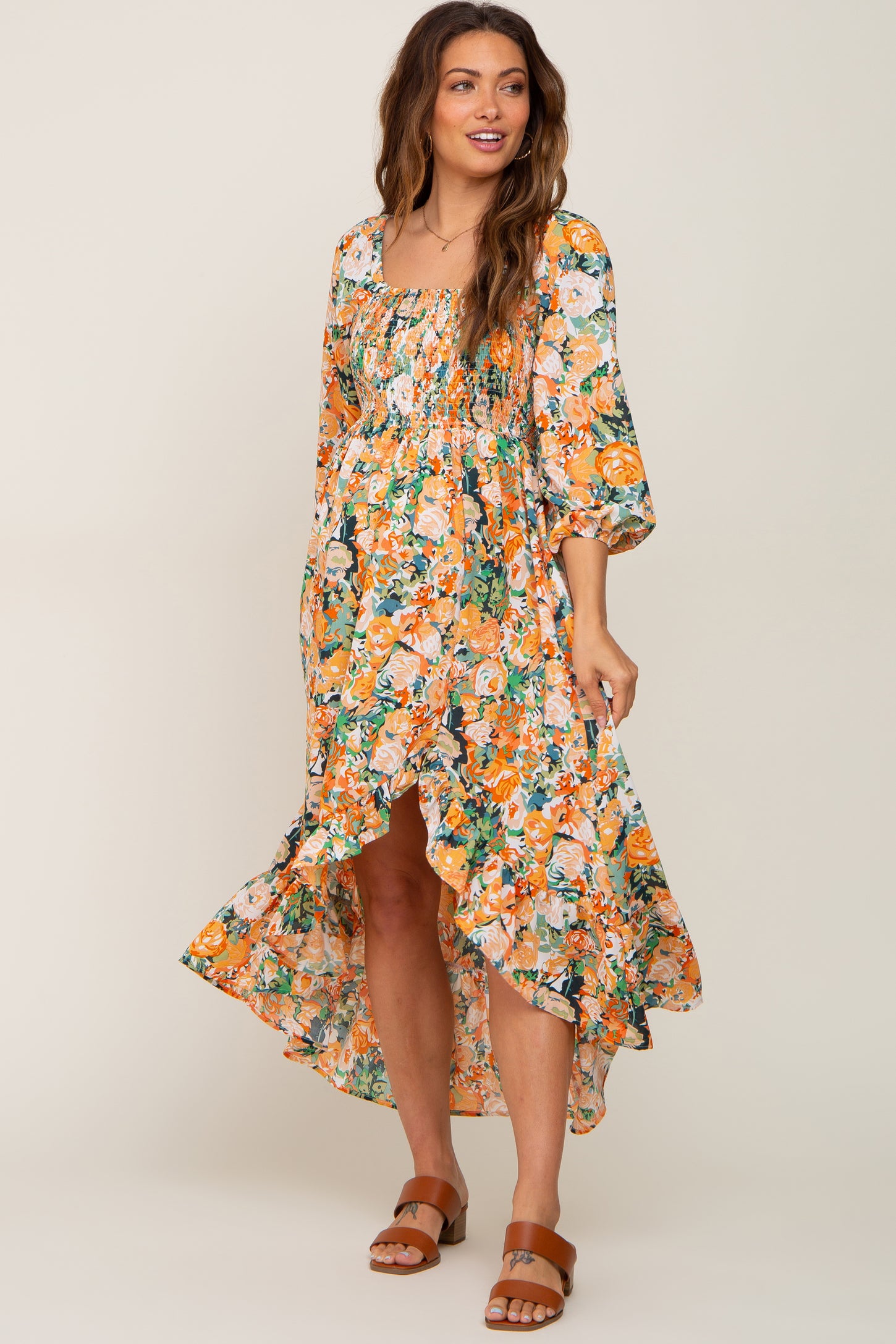woman wearing orange floral smocked high-low maternity midi dress with brown sandals