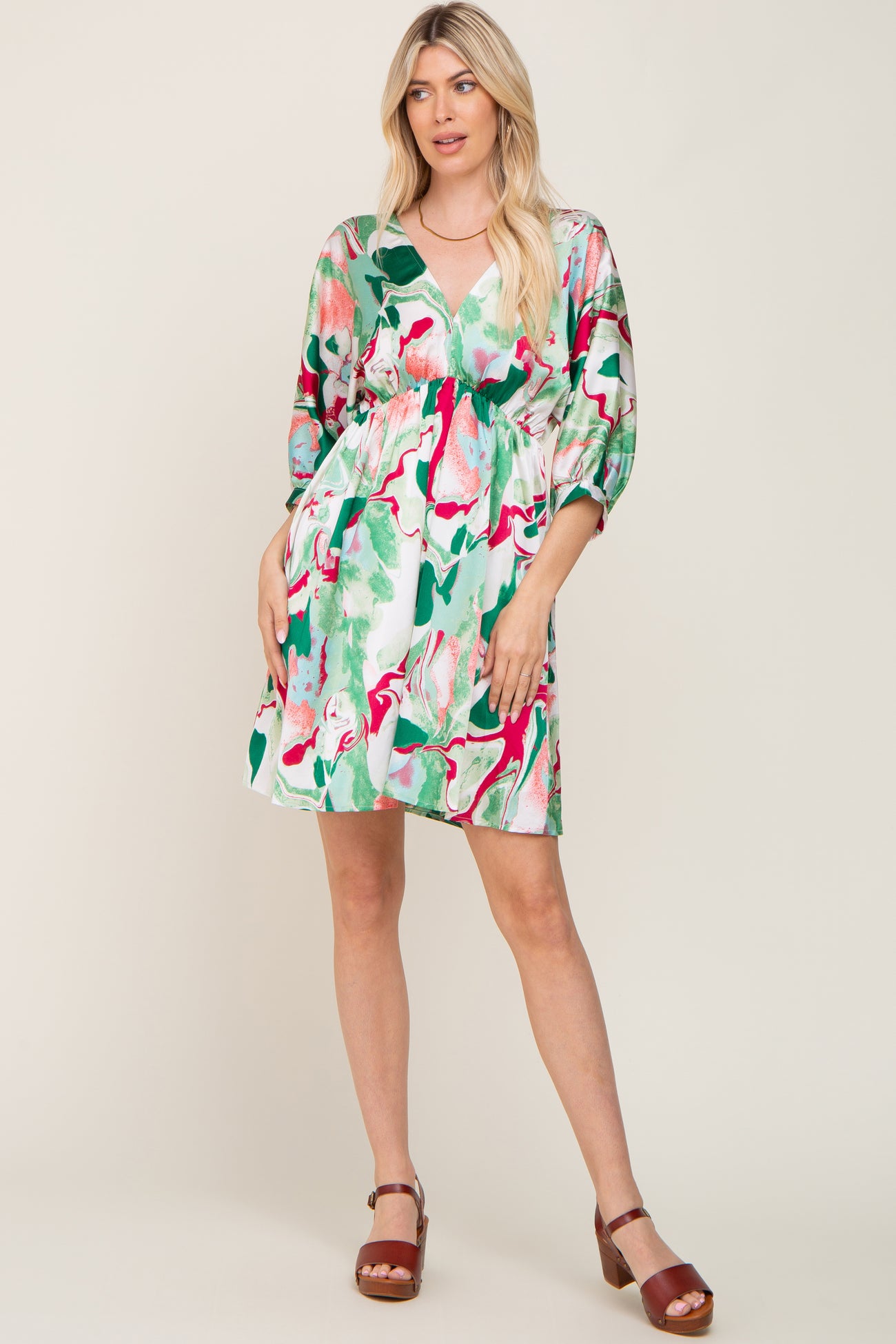 Woman wearing a green and pink marble print v-neck mini dress with three-quarter sleeves and brown sandals