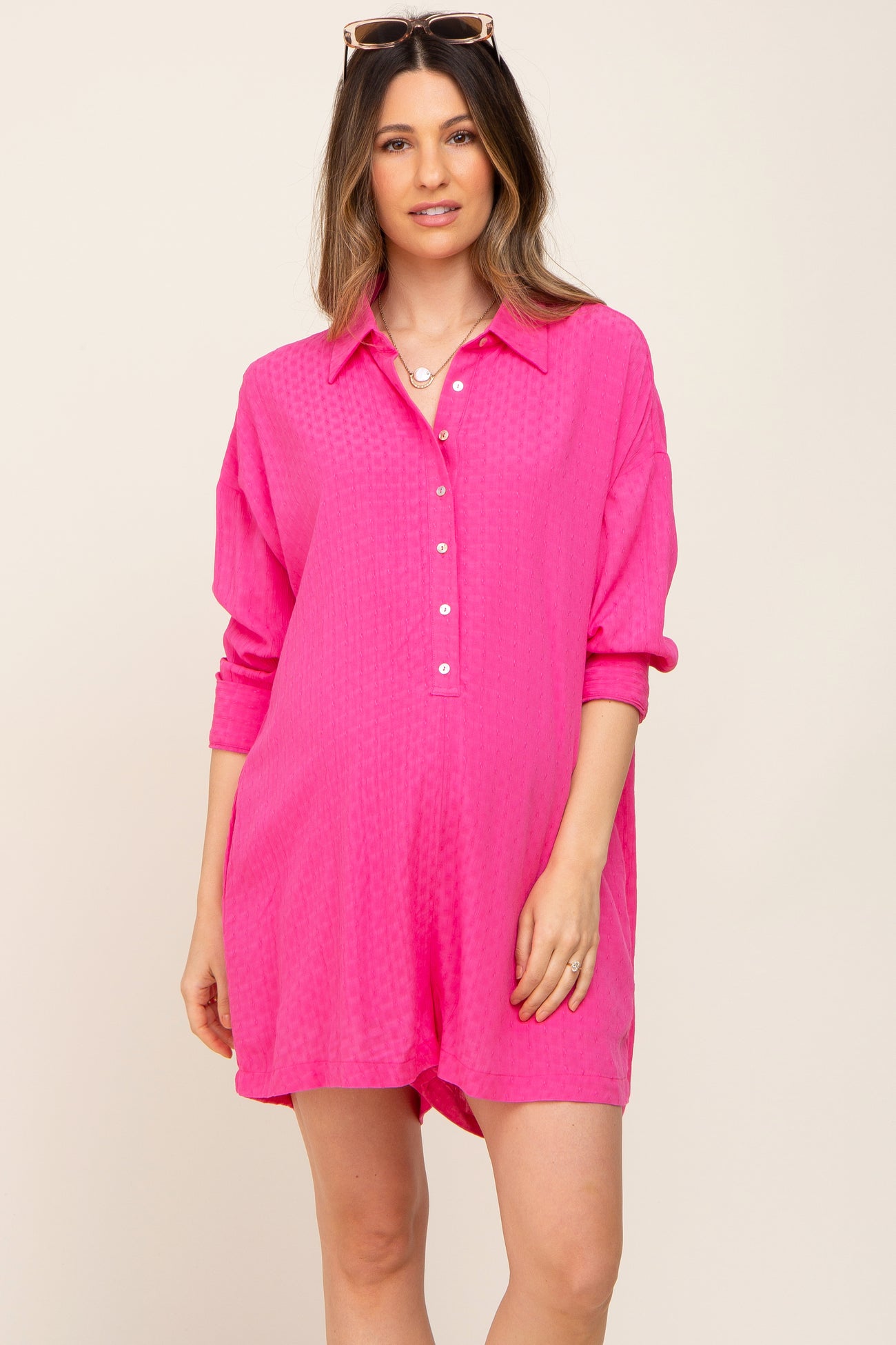 Woman wearing a bright pink button-down romper with long sleeves and a collar against a neutral background