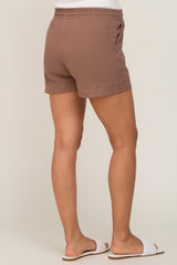 Back view of woman wearing brown linen shorts with elastic waistband and white slide sandals