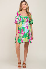 woman wearing a vibrant green floral maternity dress with puff sleeves and a fitted bodice, showcasing her baby bump