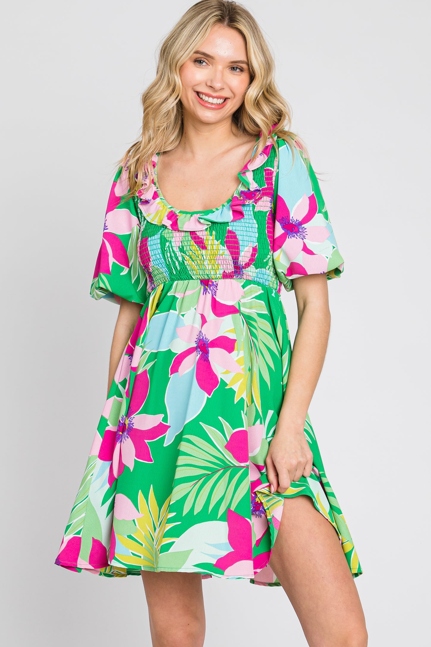 woman wearing a green floral short dress with pink and white flowers and puff sleeves, smiling at the camera