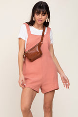 woman wearing pink muslin overalls and a brown faux crocodile leather belt bag over a white t-shirt