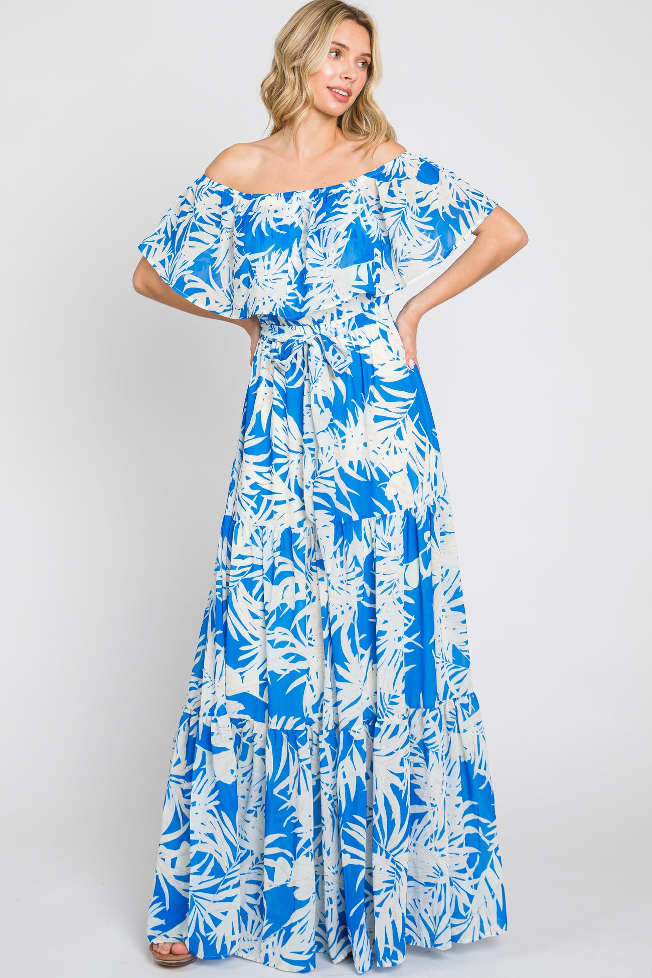 woman wearing a blue and white off-the-shoulder maxi dress with a floral pattern and ruffled sleeves