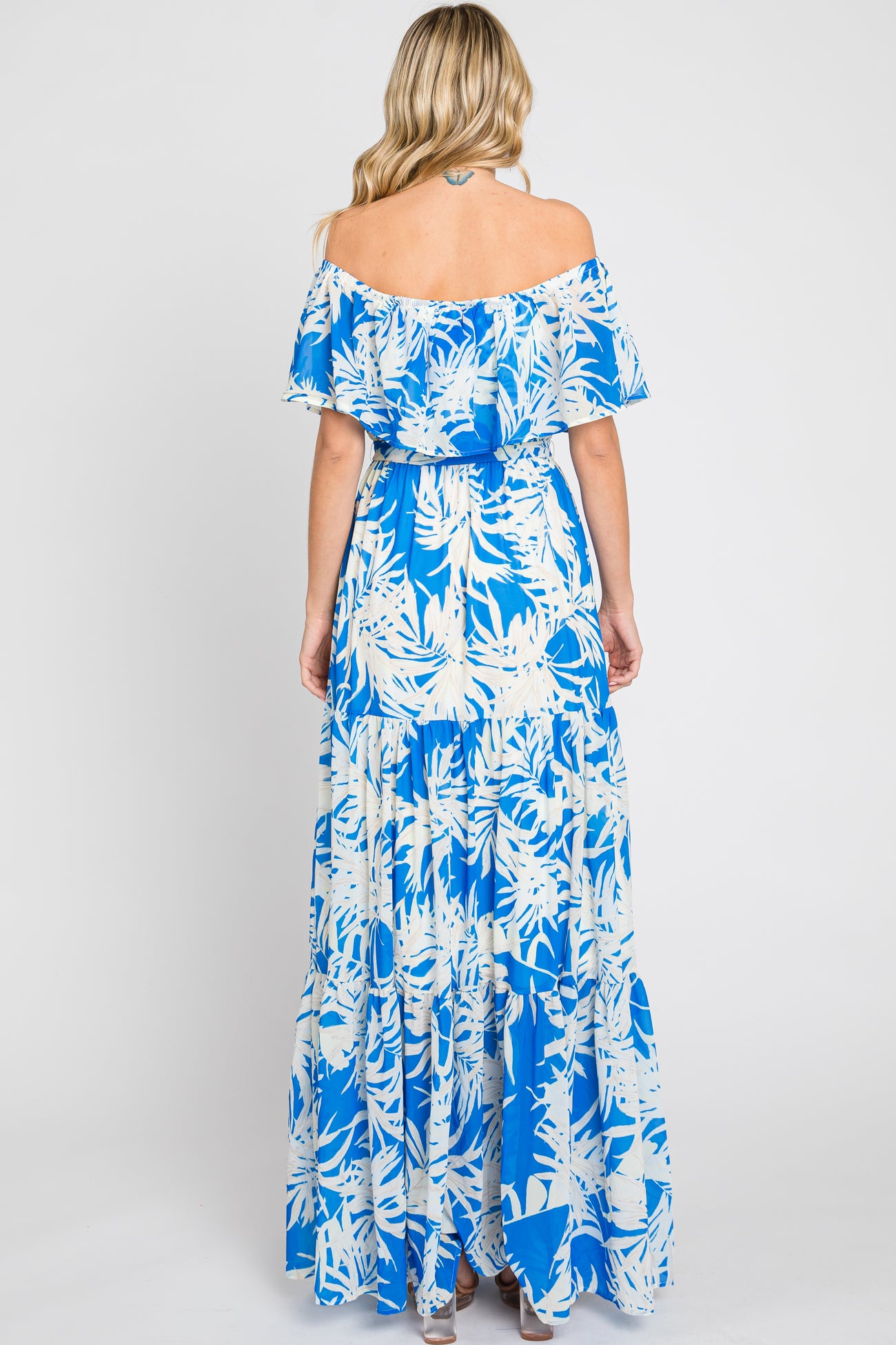 woman wearing a blue and white floral off-the-shoulder maxi dress, showing a flowing skirt and tiered design from the back
