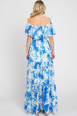 woman wearing a blue and white floral off-the-shoulder maxi dress, showing a flowing skirt and tiered design from the back