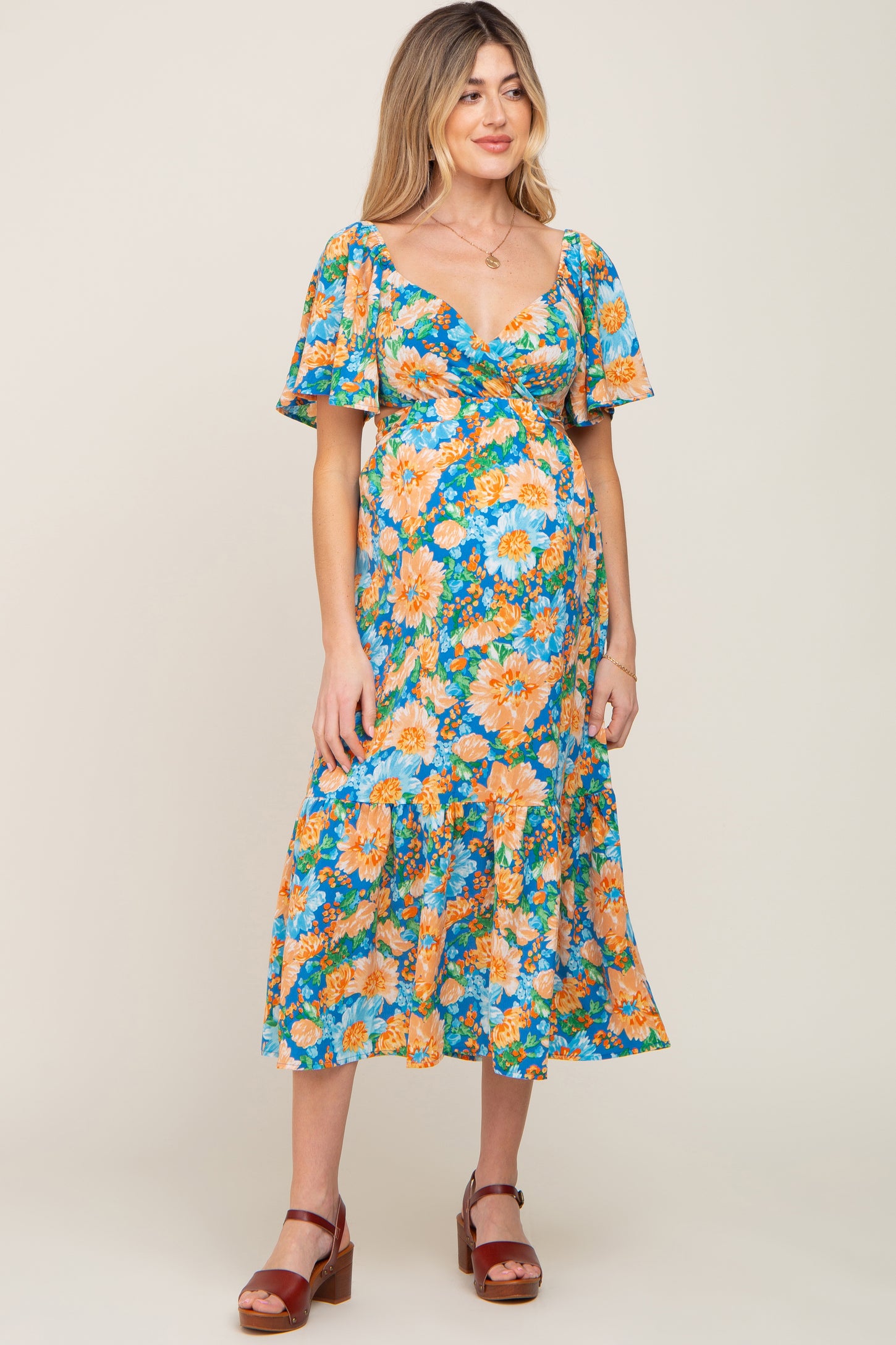 woman wearing a floral maternity dress with flutter sleeves and a ruffled hem, showcasing her baby bump
