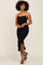 woman wearing a black ruched midi dress with adjustable straps and a side slit, styled with heeled sandals