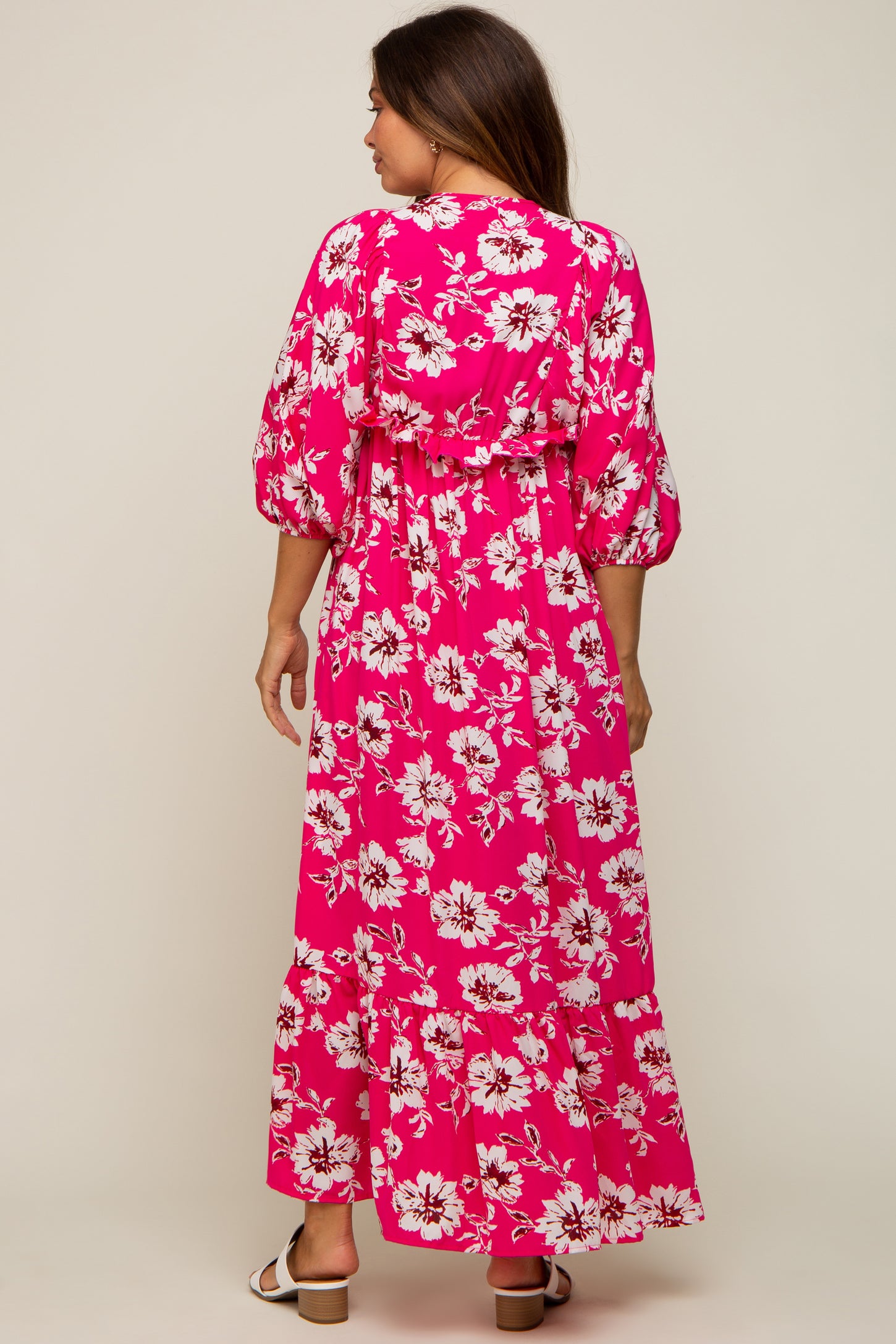 woman wearing a pink floral maternity maxi dress with puffed sleeves and a fitted waist, showing her baby bump from the back