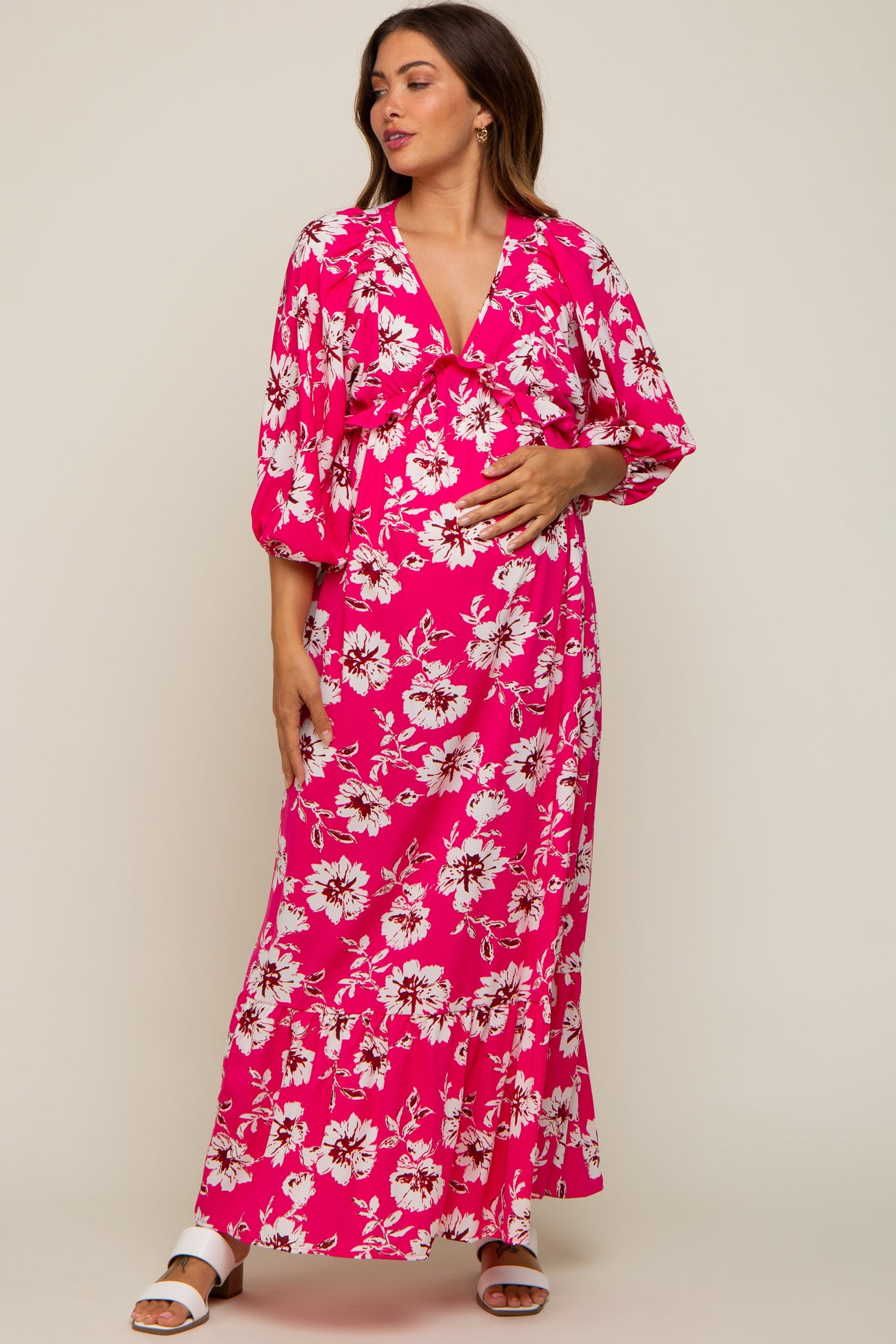 woman wearing a pink floral maternity maxi dress with a deep v-neck and ruffled hem, holding her baby bump