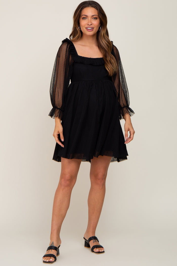 Pregnant woman wearing a black mesh long sleeve maternity mini dress with ruffle details and black heels