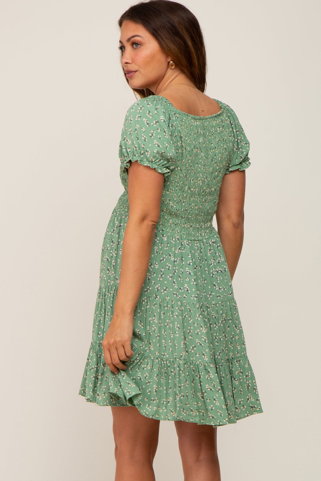 woman wearing a green floral smocked maternity mini dress with puff sleeves and tiered skirt