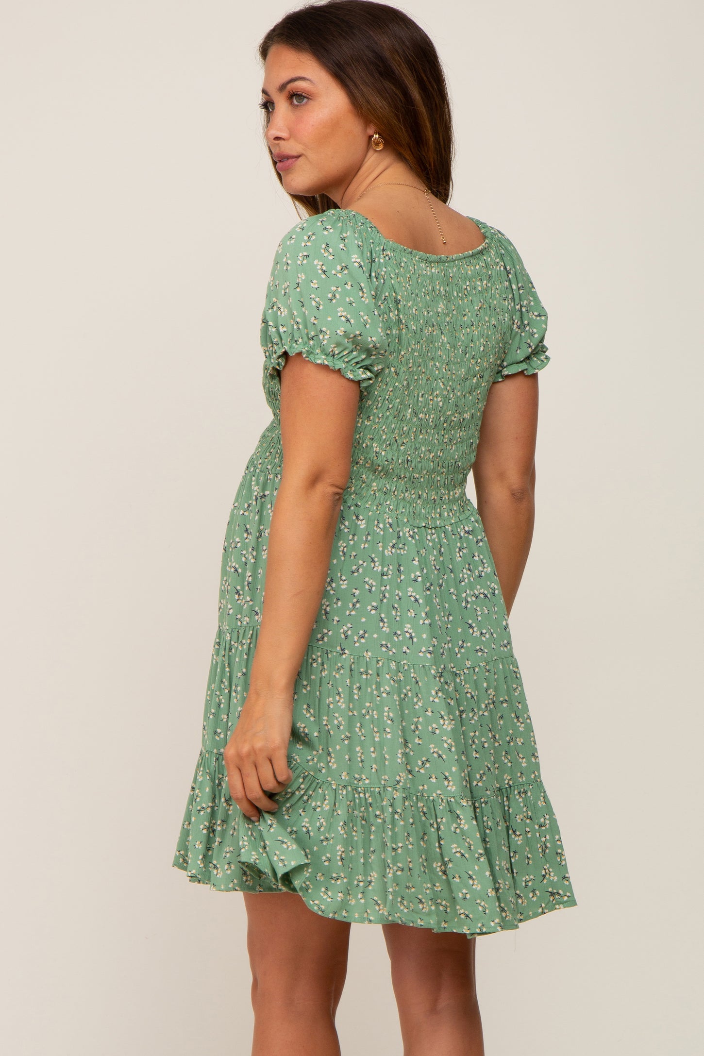 woman wearing a green floral smocked maternity mini dress with puff sleeves and tiered skirt