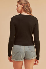 Back view of a woman wearing a black long sleeve ribbed knit top and light wash denim shorts
