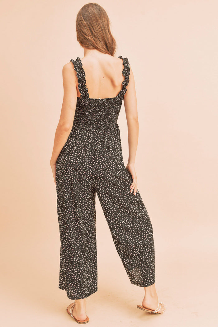 Woman from behind wearing a black floral smocked jumpsuit with ruffle straps and wide legs