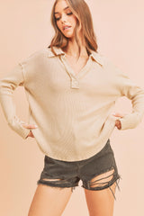 woman wearing a beige long sleeve waffle knit polo shirt and distressed black denim shorts