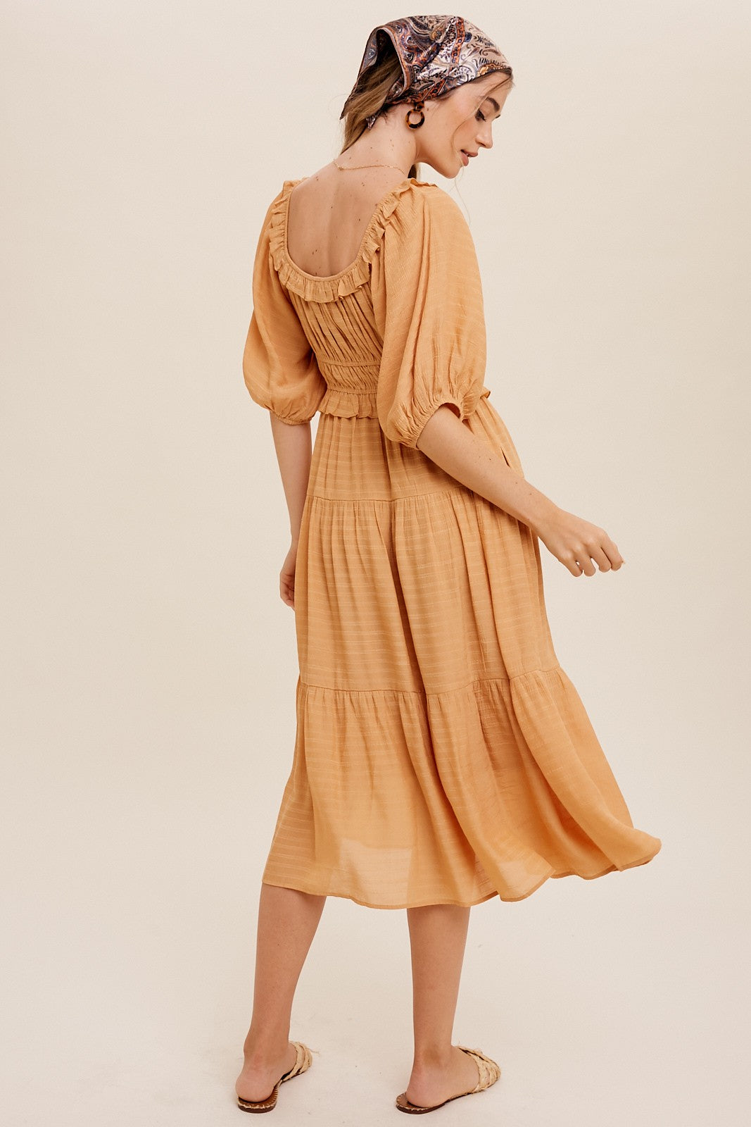 Woman wearing a mustard yellow tiered midi dress with puff sleeves and a patterned headscarf