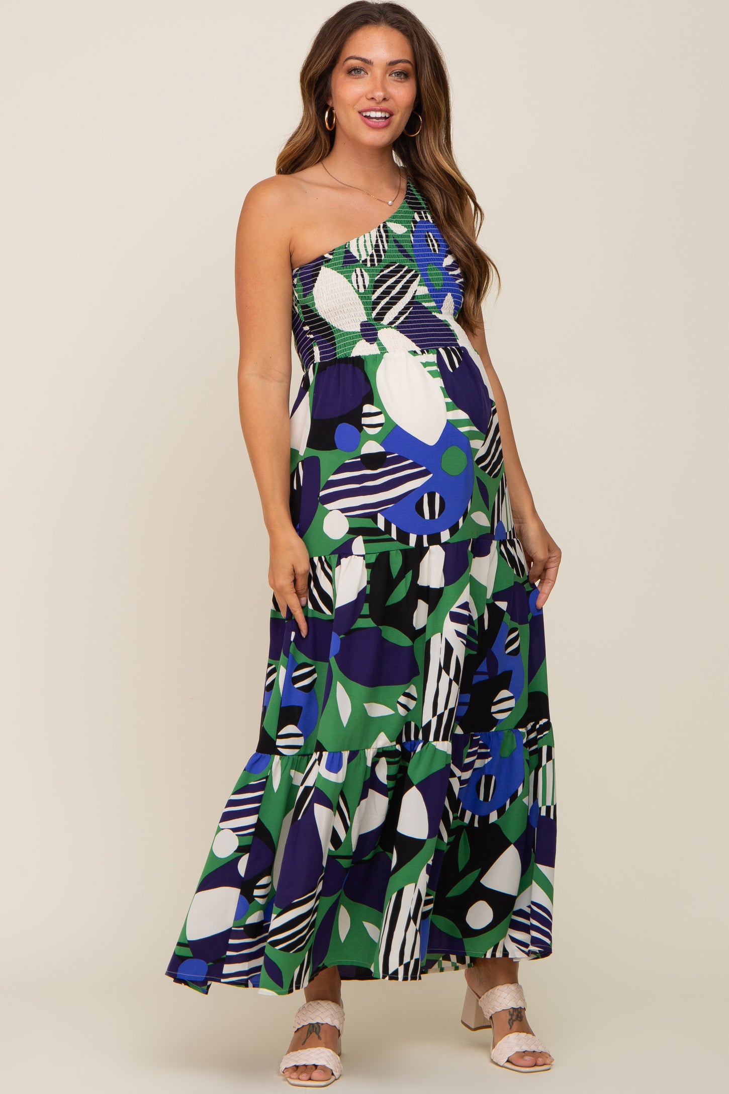 woman wearing a colorful one-shoulder maternity maxi dress with abstract patterns and showing her baby bump