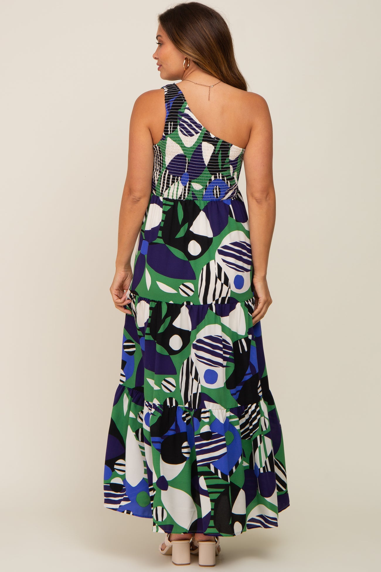 woman wearing a patterned one-shoulder maternity maxi dress with a tiered skirt, showing off a baby bump