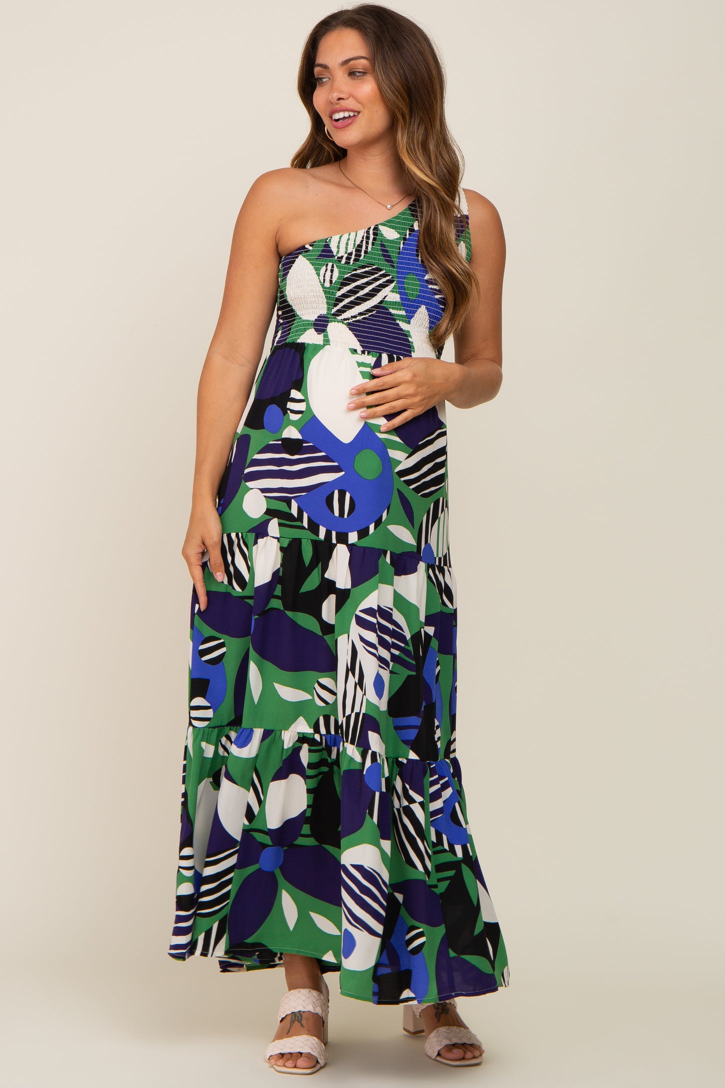 woman wearing a colorful one-shoulder maternity maxi dress with a tiered skirt and abstract patterns