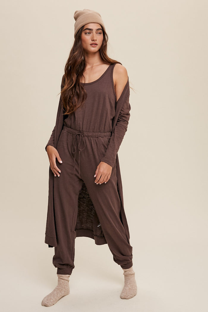 woman wearing brown lounge set with matching cardigan, beanie, and socks against a neutral background