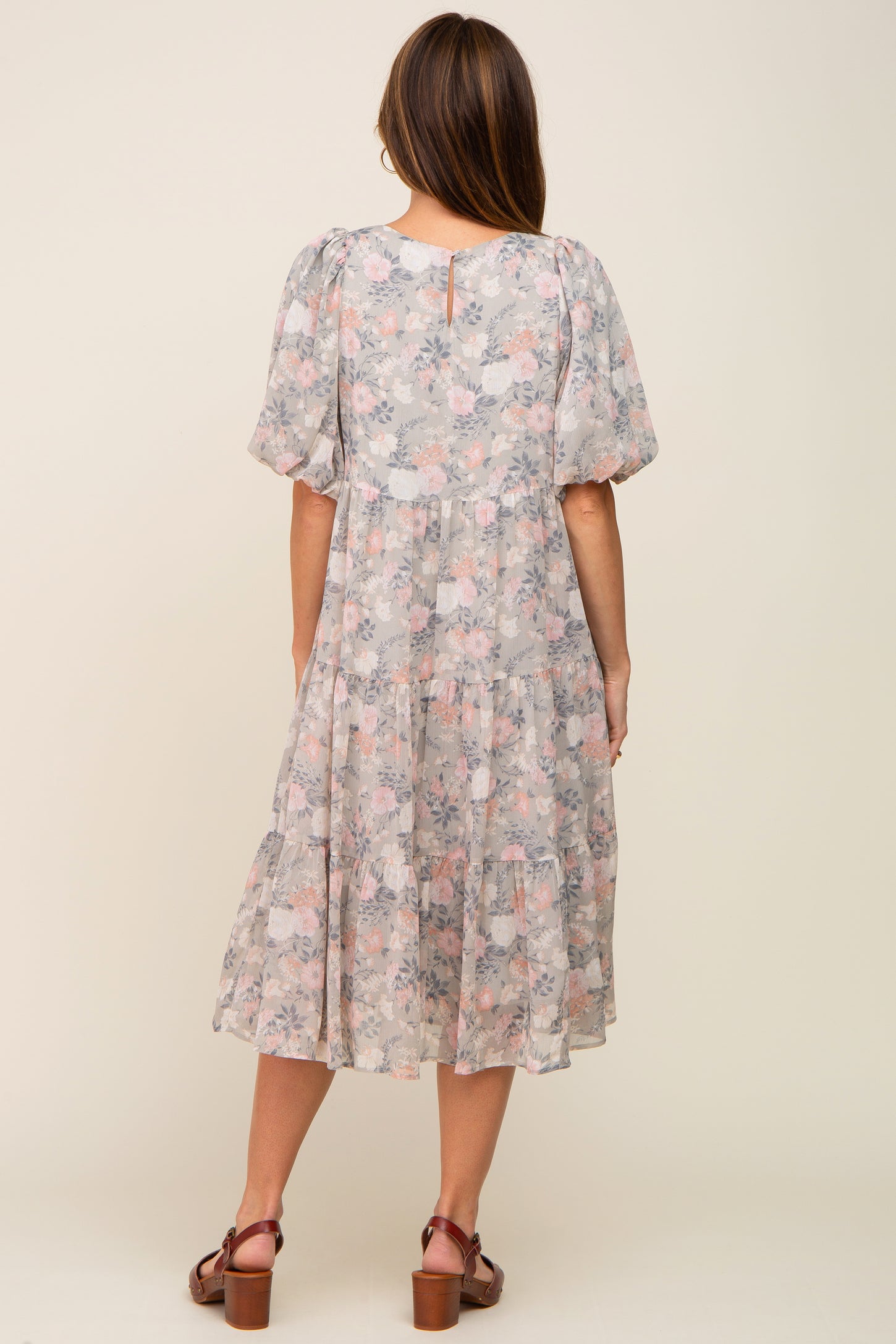 Back view of a woman wearing a grey floral tiered midi dress with puff sleeves and brown clogs