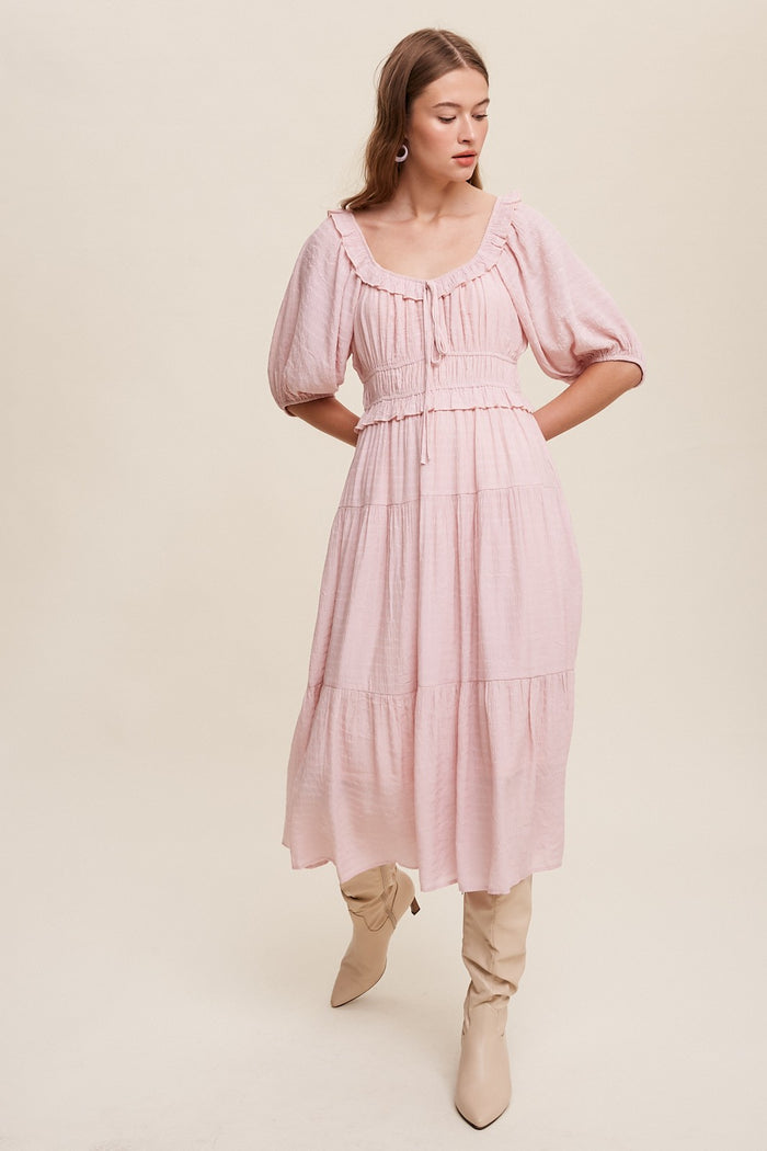 Woman wearing a light pink midi dress with puff sleeves and tiered skirt paired with beige knee-high boots