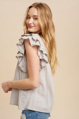 Woman wearing a grey sleeveless top with ruffle eyelet trim and denim shorts against a beige background