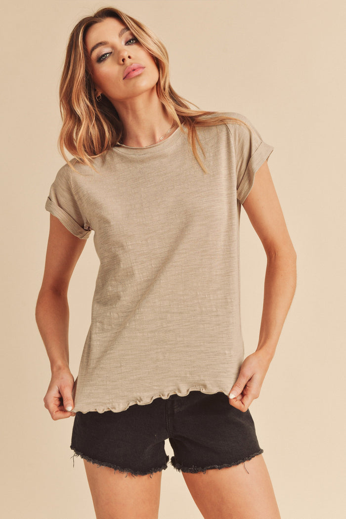 Woman wearing a beige short sleeve slub knit t-shirt and black denim shorts against a neutral background