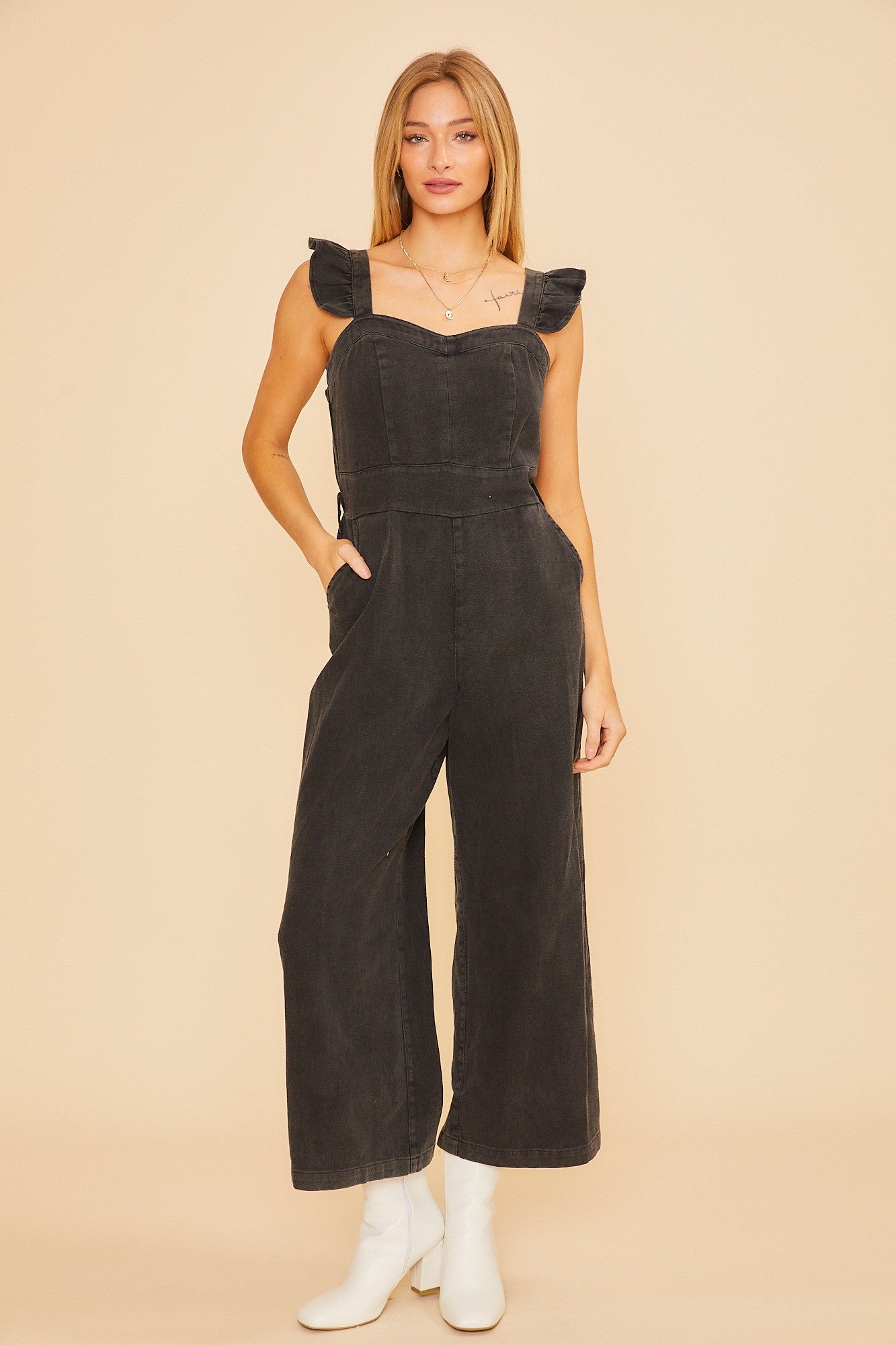 woman wearing a black denim jumpsuit with ruffle straps and wide legs paired with white boots