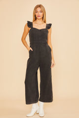 woman wearing a black denim jumpsuit with ruffle straps and wide legs paired with white boots