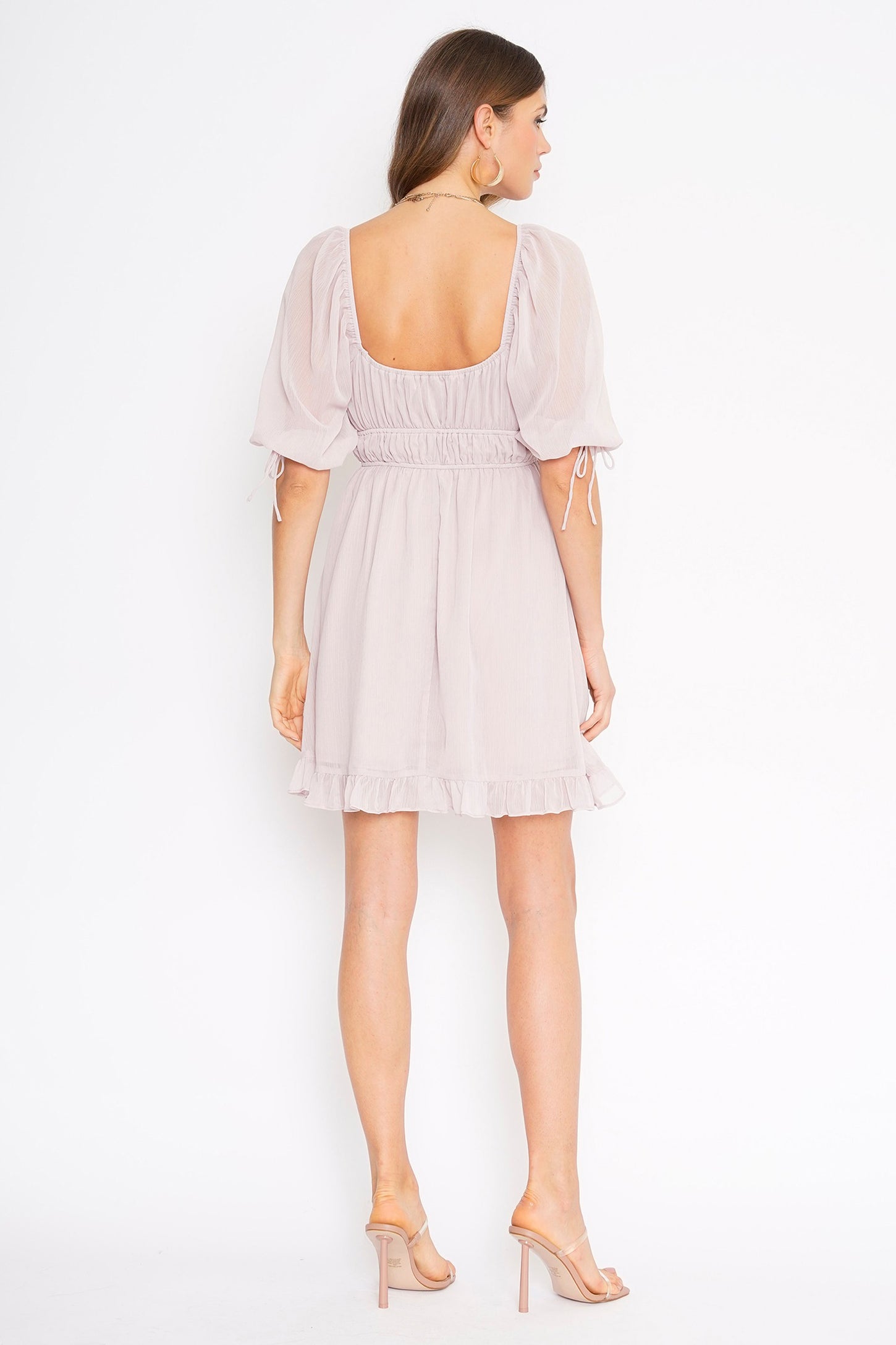 Back view of a woman wearing a light purple puff sleeve mini dress with a square neckline and ruffled hem