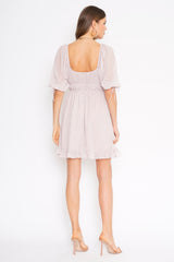 Back view of a woman wearing a light purple puff sleeve mini dress with a square neckline and ruffled hem