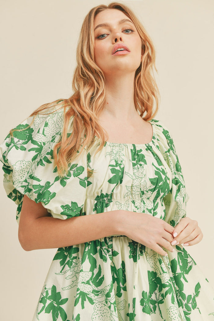 Woman wearing a cream puff sleeve dress with a green floral print and square neckline