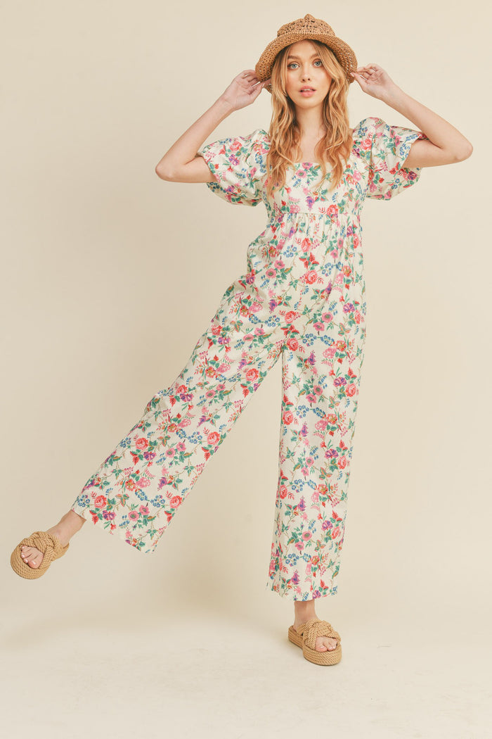 Woman wearing a floral puff sleeve jumpsuit with a straw hat and woven platform sandals