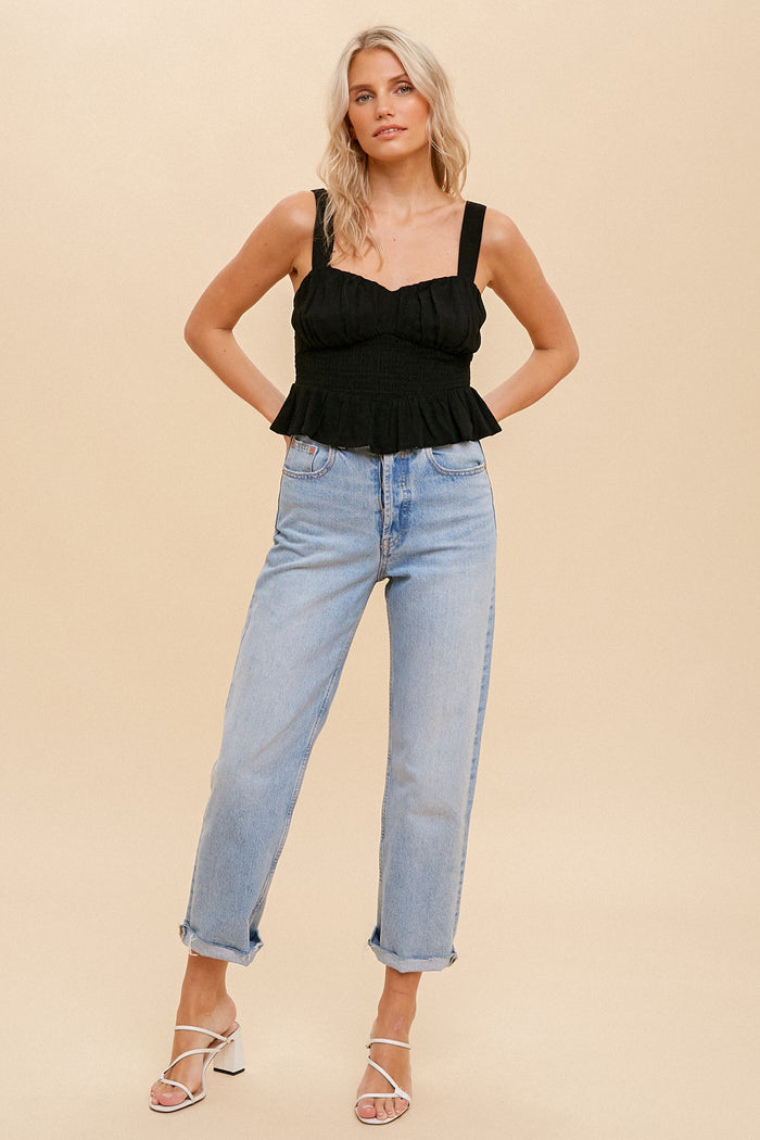 woman wearing a black smocked peplum tank top and light wash straight leg jeans with white strappy heels