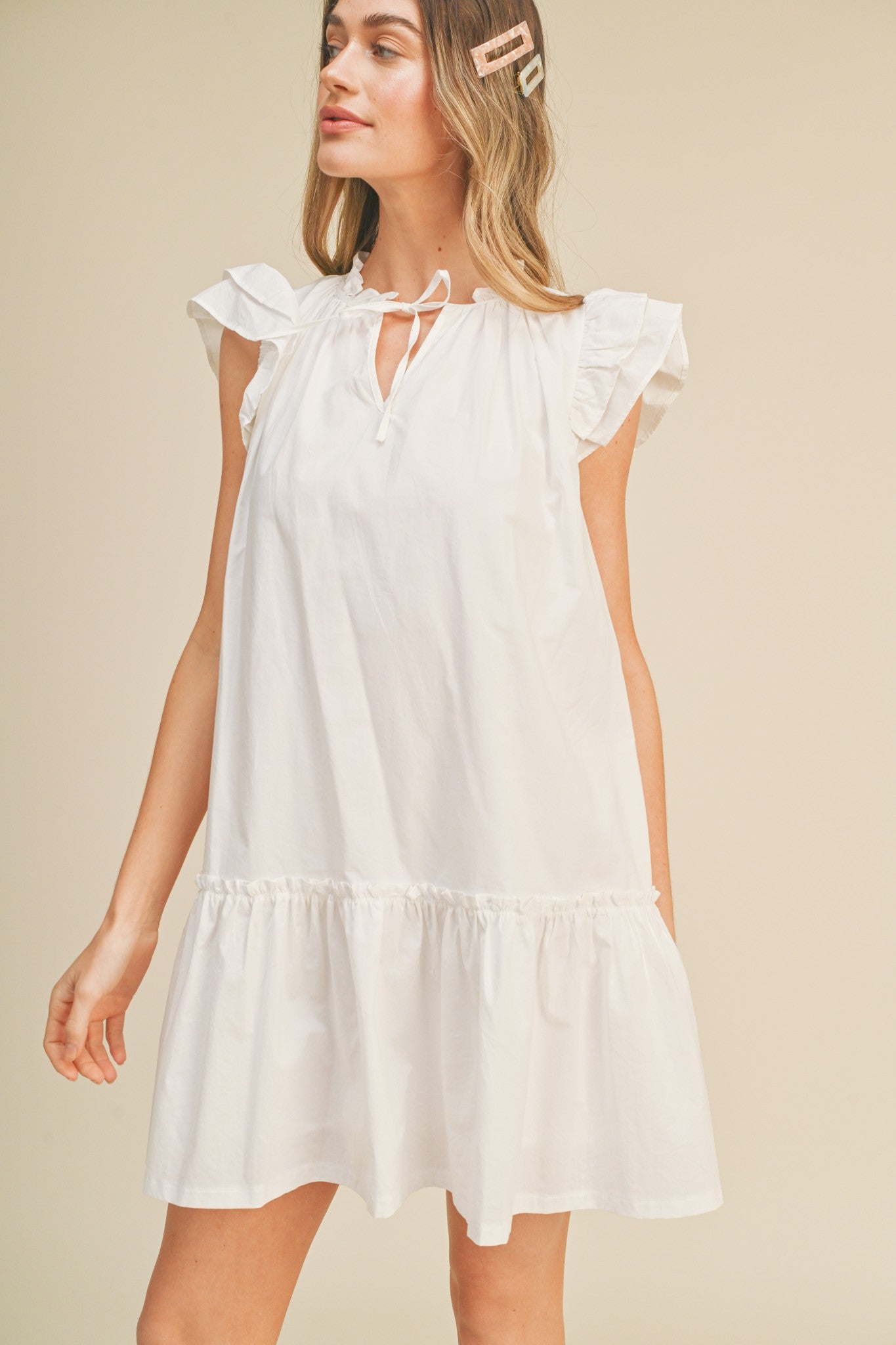 woman wearing a white short sleeve mini dress with ruffle details and a tie neck