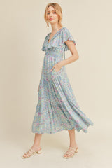 woman wearing a light blue floral maxi dress with ruffle sleeves and pockets, standing against a neutral background