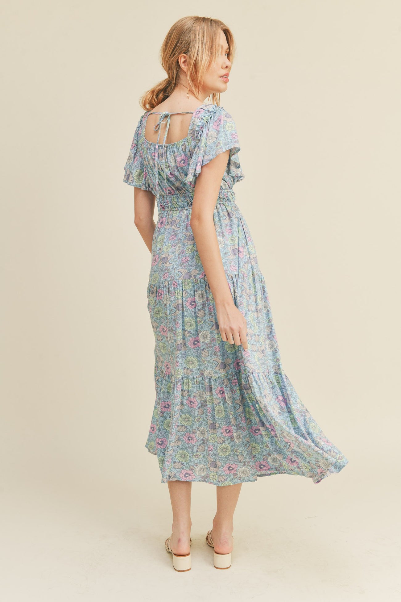 woman wearing a floral blue maxi dress with ruffled sleeves and a keyhole back detail