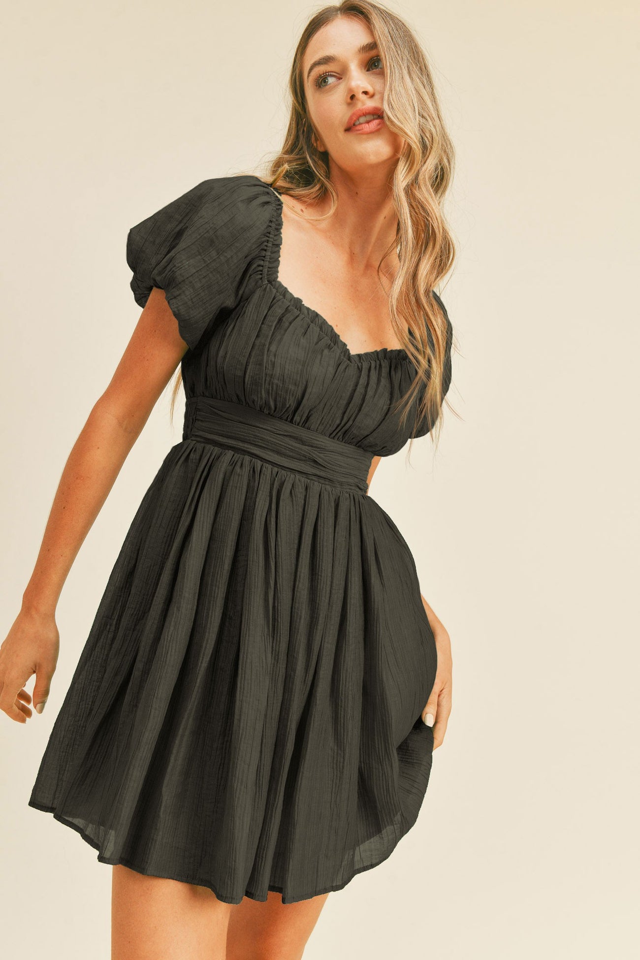 woman wearing a black puff sleeve mini dress with a fitted waist and a flared skirt