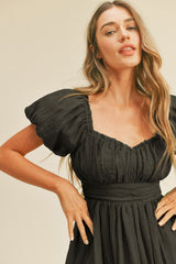 woman wearing a black puff sleeve dress with a fitted waist and gathered bodice