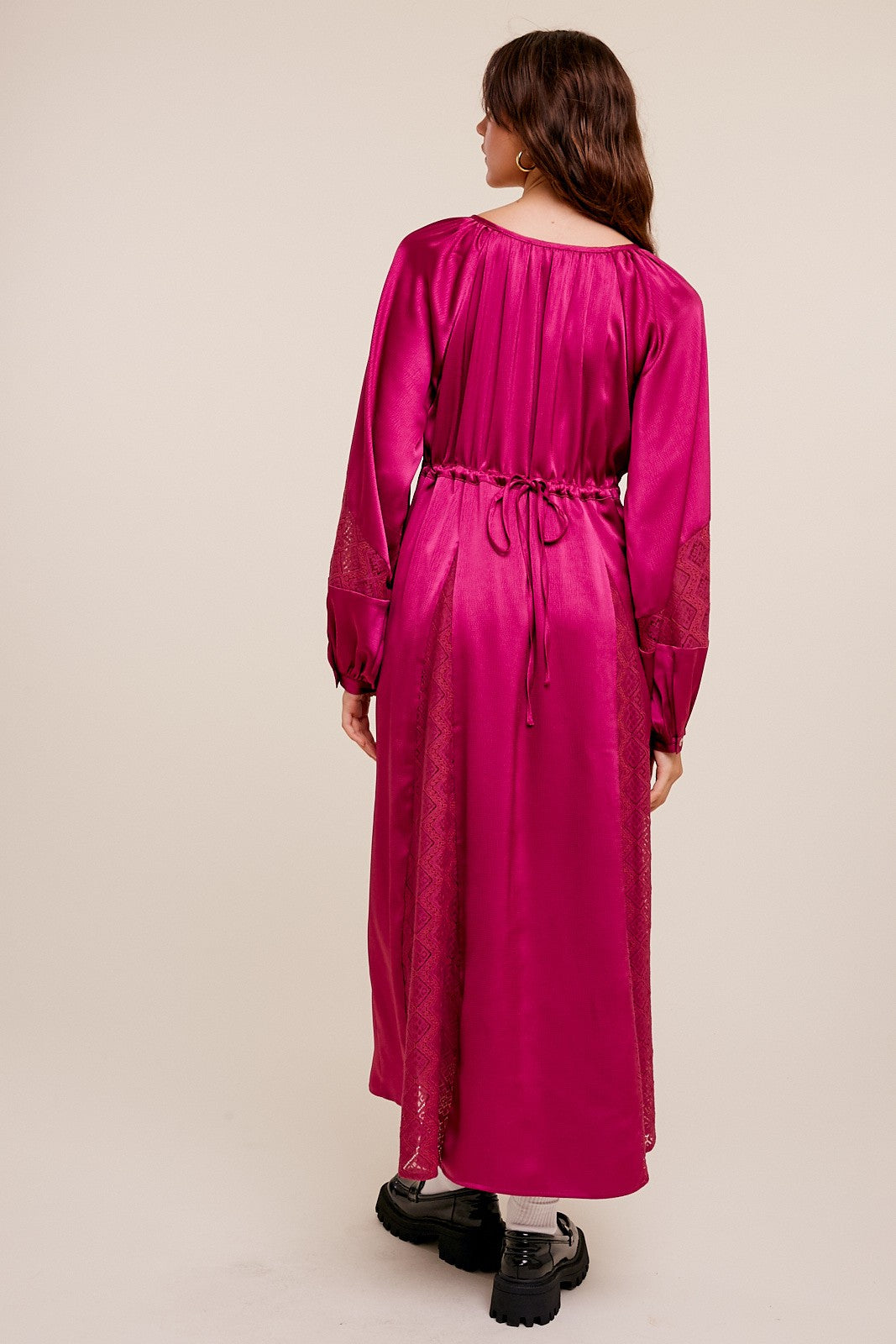 Woman from behind wearing a long-sleeved magenta satin maxi dress with lace panels and a drawstring waist