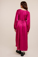 Woman from behind wearing a long-sleeved magenta satin maxi dress with lace panels and a drawstring waist