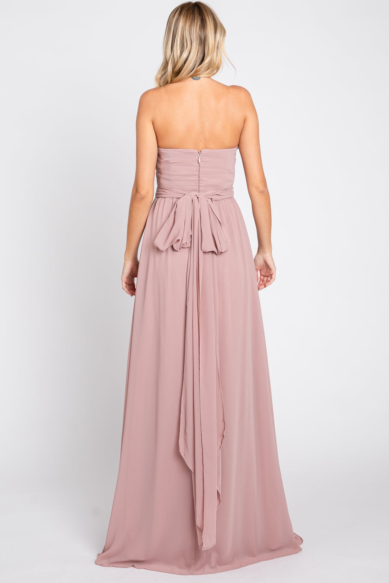 woman wearing a blush strapless maxi dress with a tied bow detail at the back